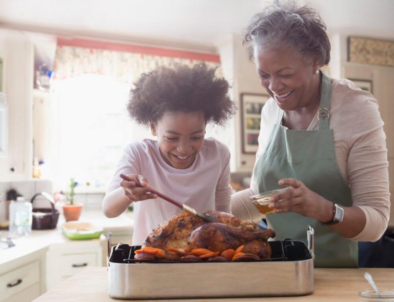 Elder and young woman preparing poultry dish together.